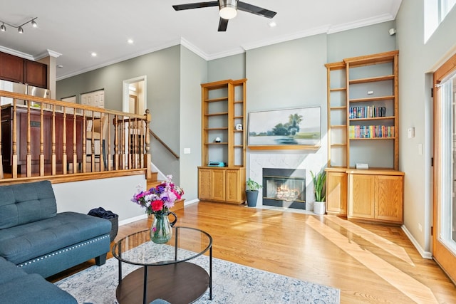 living room with crown molding, a fireplace, light wood-type flooring, and baseboards