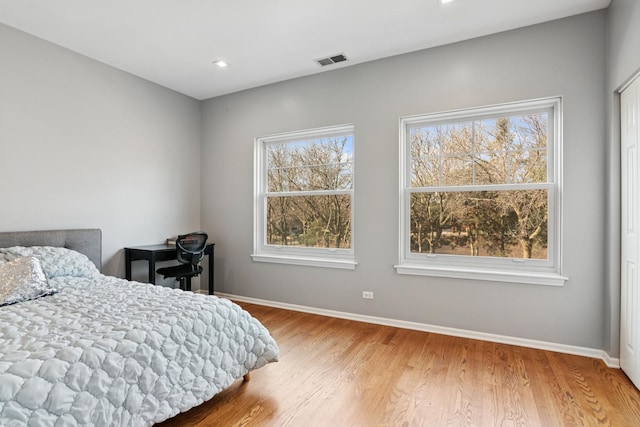 bedroom with multiple windows, wood finished floors, visible vents, and baseboards