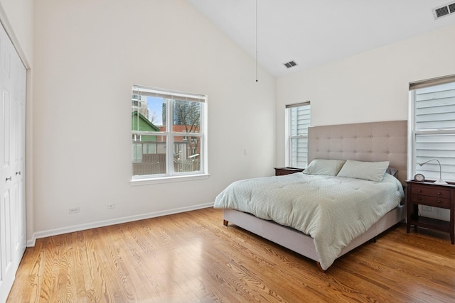 bedroom with visible vents, baseboards, high vaulted ceiling, and wood finished floors