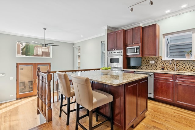 kitchen featuring backsplash, a kitchen island, ornamental molding, stainless steel appliances, and a sink