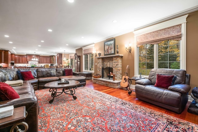 living room featuring hardwood / wood-style flooring, ornamental molding, and a stone fireplace