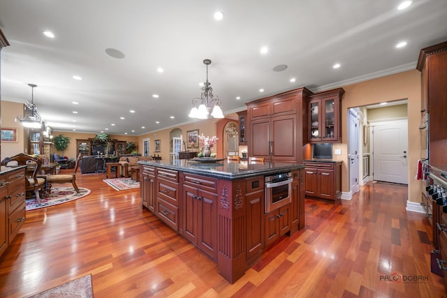 kitchen featuring a kitchen island with sink, hanging light fixtures, hardwood / wood-style flooring, and oven