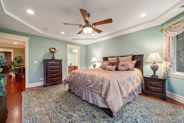 bedroom with wood-type flooring, ceiling fan, ensuite bath, and a tray ceiling