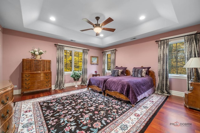 bedroom with dark hardwood / wood-style floors, ceiling fan, and a tray ceiling