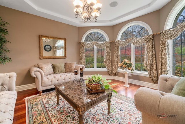 interior space with a notable chandelier, wood-type flooring, and a raised ceiling