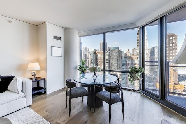 dining room with visible vents, a view of city, wood finished floors, and floor to ceiling windows