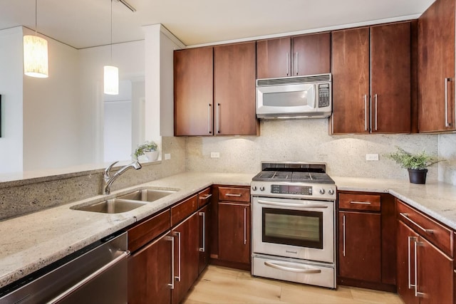 kitchen featuring a sink, light stone counters, backsplash, appliances with stainless steel finishes, and hanging light fixtures