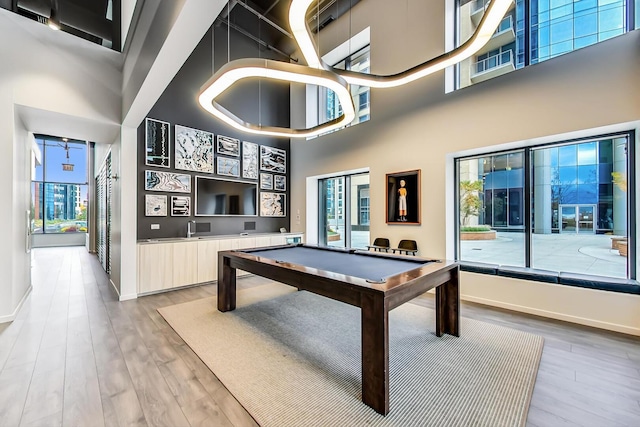 rec room with light wood-style floors and a towering ceiling