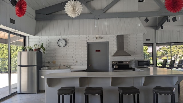kitchen with a sink, wall chimney range hood, light countertops, stainless steel appliances, and a breakfast bar area