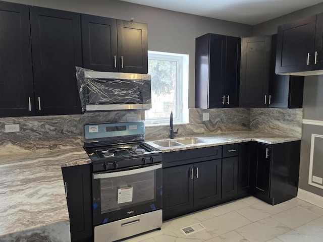 kitchen featuring marble finish floor, a sink, dark cabinetry, stainless steel appliances, and decorative backsplash