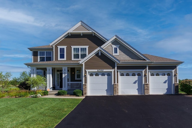 craftsman-style home with a garage, aphalt driveway, a front yard, and covered porch