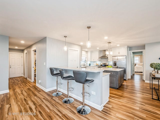 kitchen with light wood finished floors, stainless steel fridge, stove, light countertops, and wall chimney range hood