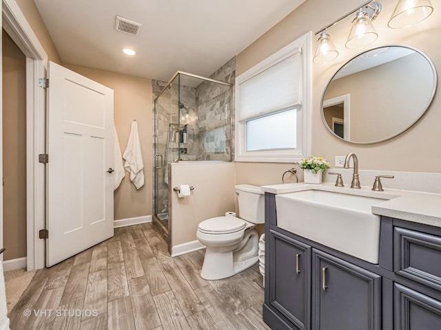 bathroom with toilet, wood finished floors, vanity, baseboards, and a shower stall