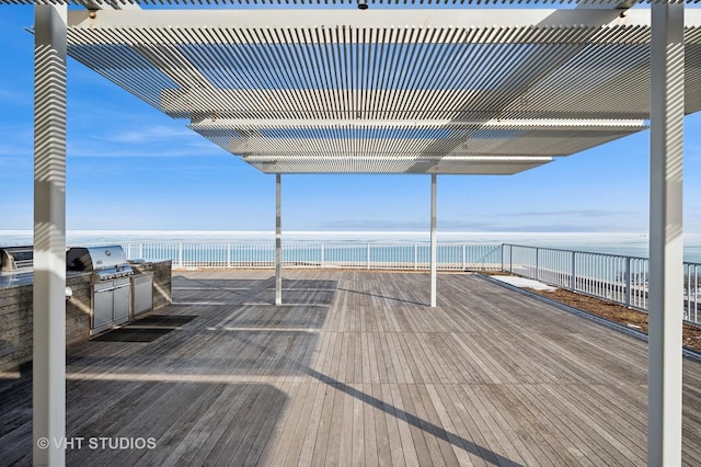 wooden deck with a water view, a grill, fence, and an outdoor kitchen