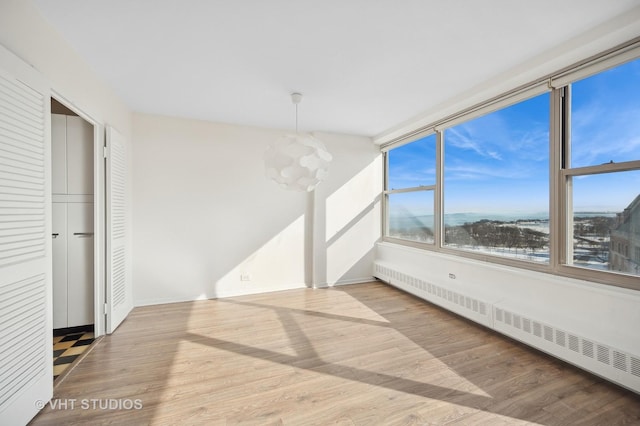 interior space with light wood-style floors, a baseboard radiator, and a notable chandelier