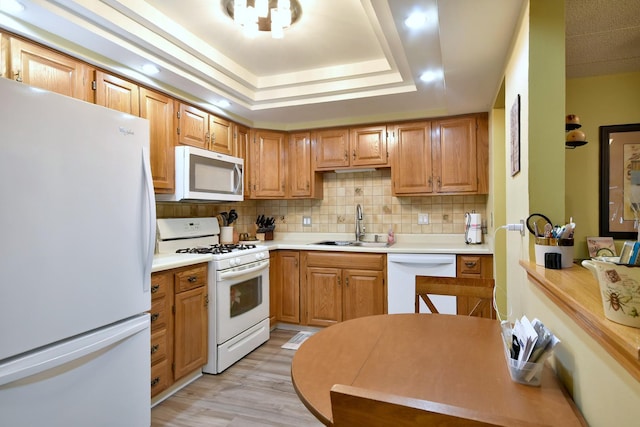 kitchen with sink, light wood-type flooring, a tray ceiling, white appliances, and decorative backsplash