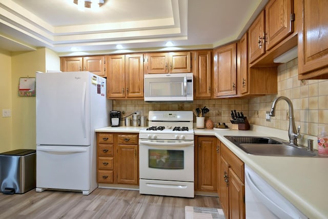 kitchen with sink, tasteful backsplash, light wood-type flooring, a raised ceiling, and white appliances