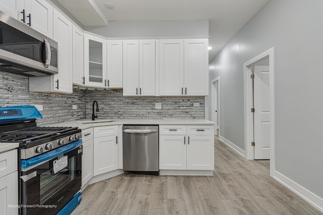 kitchen with sink, stainless steel appliances, tasteful backsplash, white cabinets, and light wood-type flooring