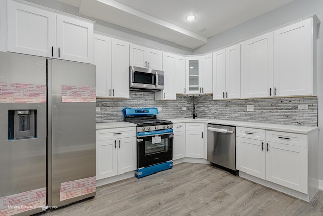 kitchen with stainless steel appliances, tasteful backsplash, white cabinets, and light hardwood / wood-style flooring