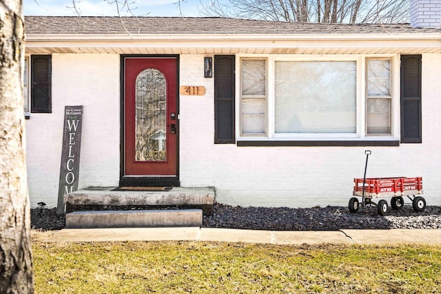 view of exterior entry featuring brick siding and roof with shingles