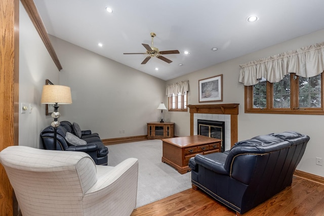 living room with a tile fireplace, ceiling fan, lofted ceiling, and wood-type flooring