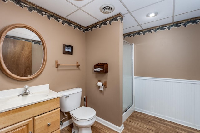 bathroom with a shower with door, toilet, wood-type flooring, a paneled ceiling, and vanity