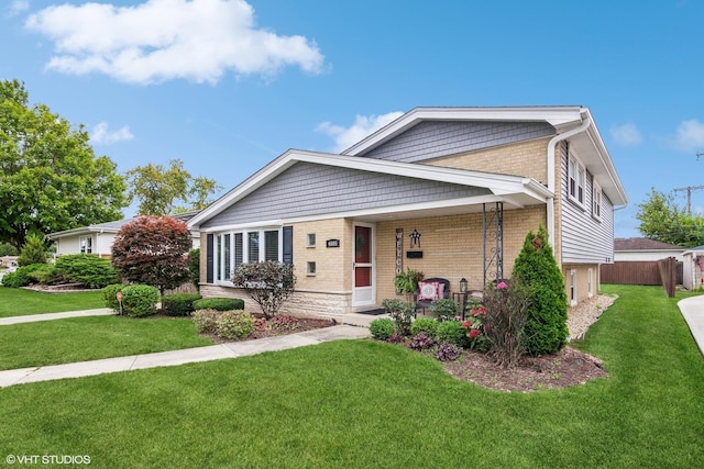 split level home featuring a front yard, fence, and brick siding
