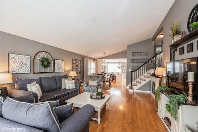 living area featuring stairway, light wood-type flooring, and vaulted ceiling