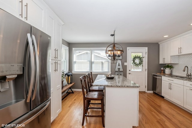 kitchen featuring tasteful backsplash, white cabinets, appliances with stainless steel finishes, a sink, and light wood finished floors