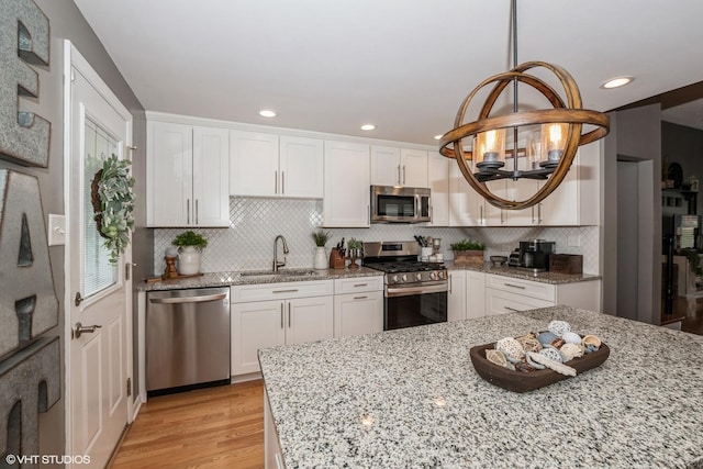 kitchen featuring light wood-type flooring, white cabinets, a chandelier, a sink, and stainless steel appliances