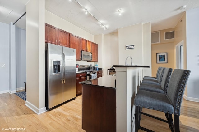 kitchen with light wood-type flooring, appliances with stainless steel finishes, a breakfast bar, and rail lighting