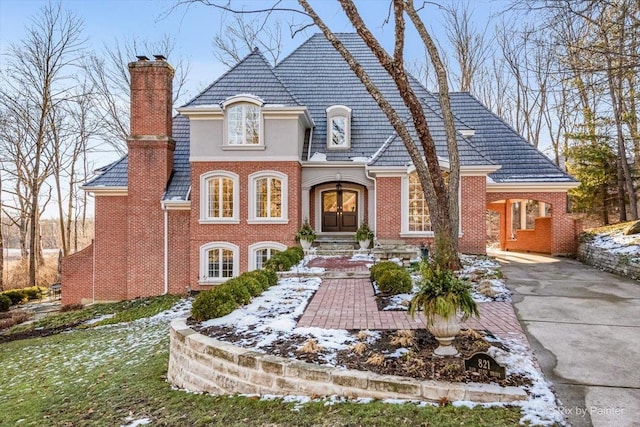 view of front of property featuring driveway, brick siding, and a chimney