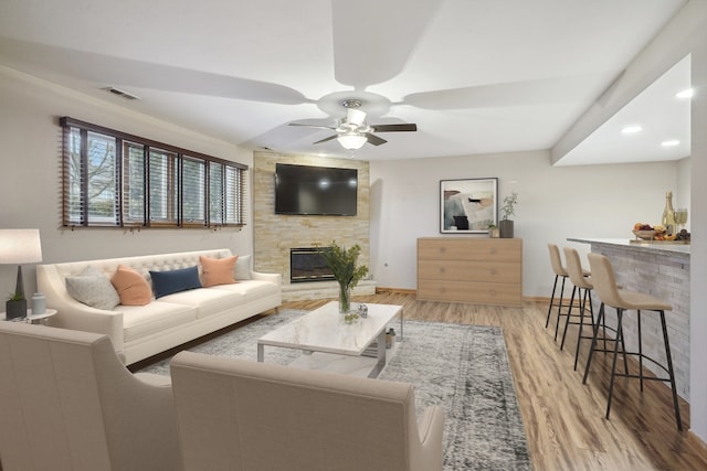 living room featuring ceiling fan, indoor bar, a fireplace, and light hardwood / wood-style floors