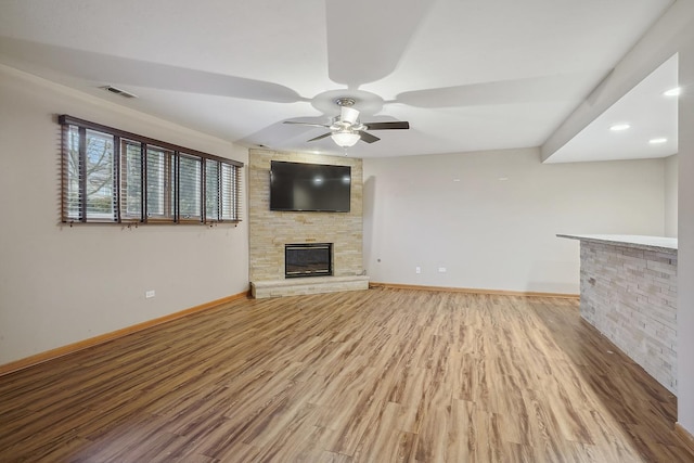 unfurnished living room featuring ceiling fan, a stone fireplace, and hardwood / wood-style floors