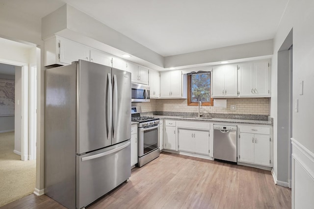 kitchen with sink, appliances with stainless steel finishes, tasteful backsplash, white cabinets, and light wood-type flooring