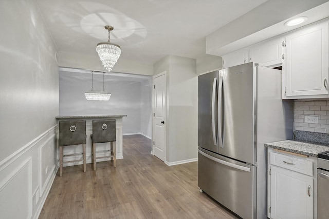 kitchen featuring decorative light fixtures, tasteful backsplash, stainless steel fridge, white cabinets, and light wood-type flooring