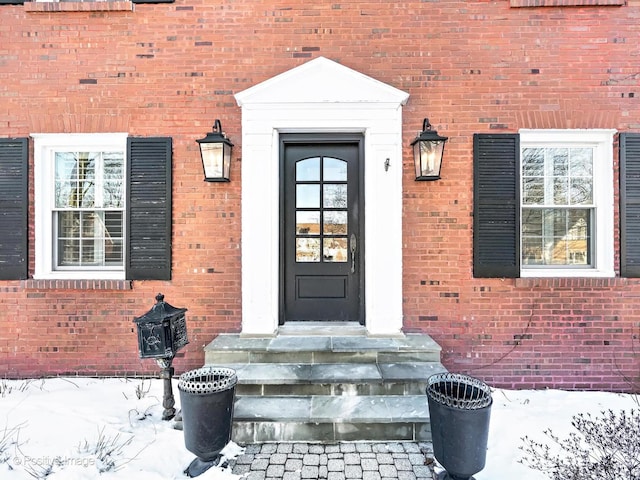 snow covered property entrance with brick siding