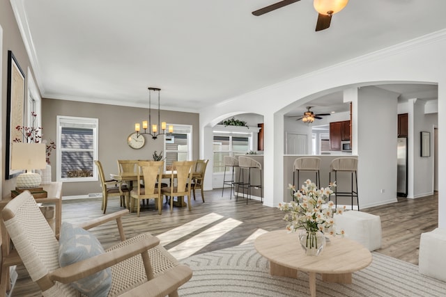 living area featuring arched walkways, ornamental molding, wood finished floors, baseboards, and ceiling fan with notable chandelier