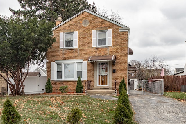 traditional-style house featuring a gate, brick siding, fence, and a front lawn