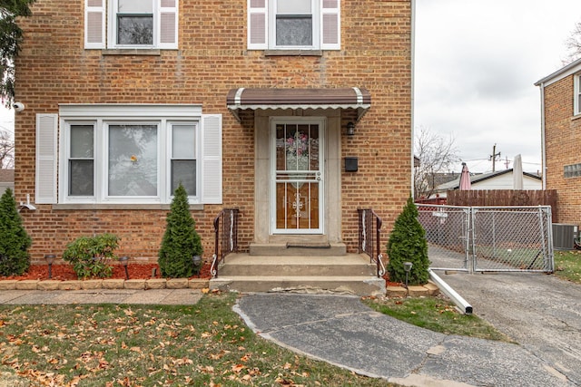 view of exterior entry with a gate, brick siding, fence, and central AC unit