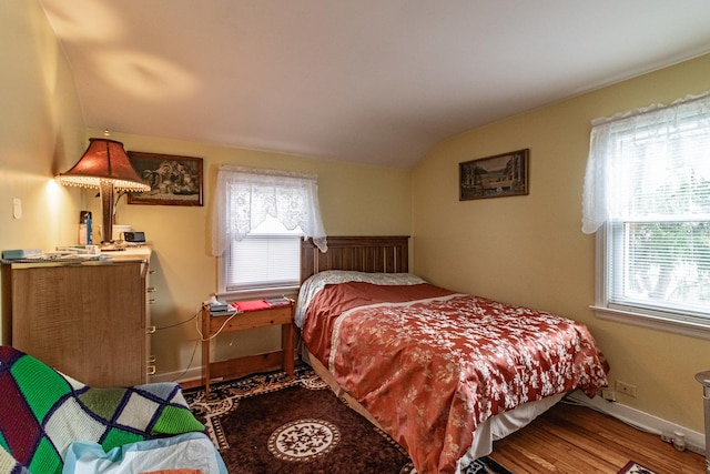 bedroom with lofted ceiling, multiple windows, baseboards, and wood finished floors