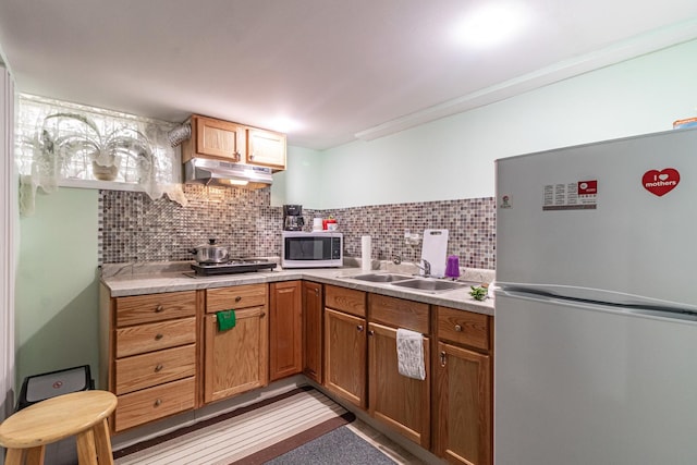 kitchen featuring under cabinet range hood, a sink, light countertops, appliances with stainless steel finishes, and backsplash