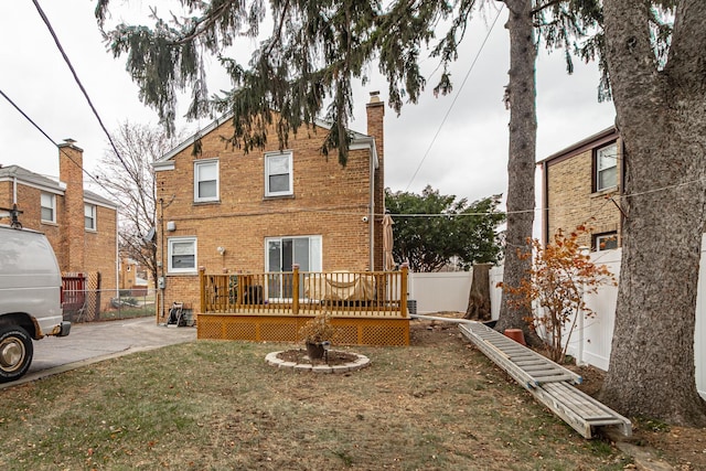 back of property featuring brick siding, fence, a yard, a wooden deck, and a chimney