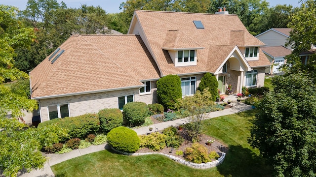 view of front of home featuring a chimney, a shingled roof, a front lawn, and brick siding