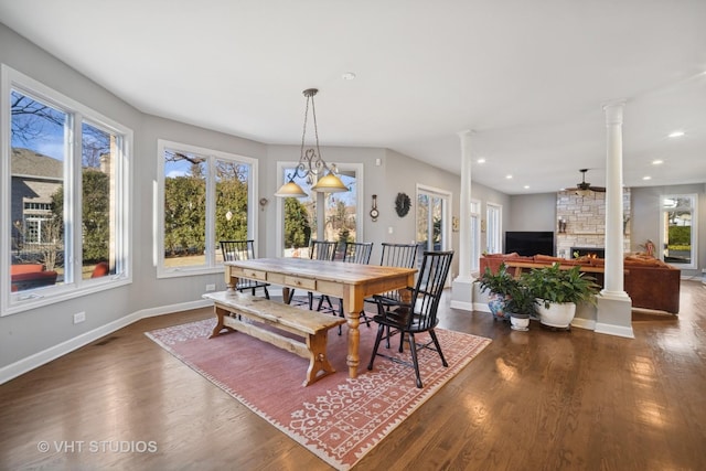 dining area featuring dark wood finished floors, recessed lighting, a stone fireplace, decorative columns, and baseboards