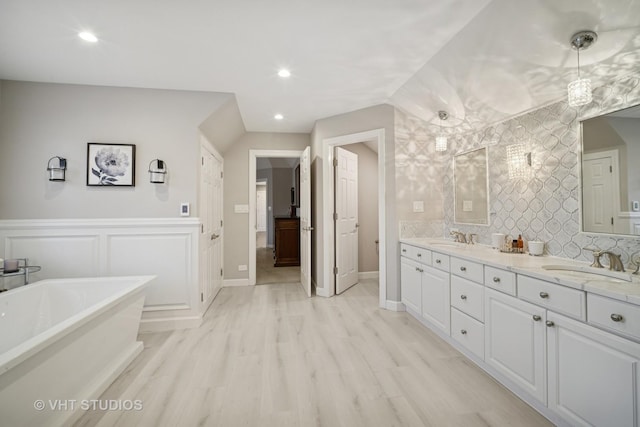 bathroom featuring wood finished floors, a wainscoted wall, a soaking tub, double vanity, and a sink