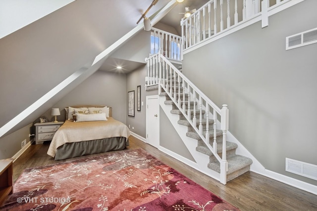 bedroom with visible vents, baseboards, a high ceiling, and wood finished floors