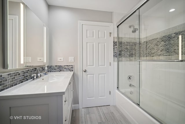 full bath featuring vanity, wood finished floors, tasteful backsplash, and bath / shower combo with glass door