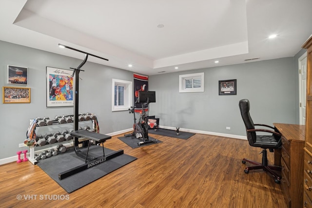 exercise room with a raised ceiling, wood finished floors, and baseboards