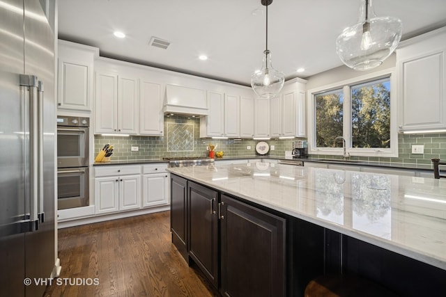 kitchen with visible vents, premium range hood, a sink, dark wood-type flooring, and appliances with stainless steel finishes